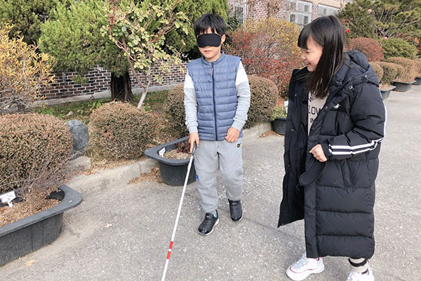 남학생이 흰지팡이를 사용하여 시각장애인 보행 체험을 하는 사진